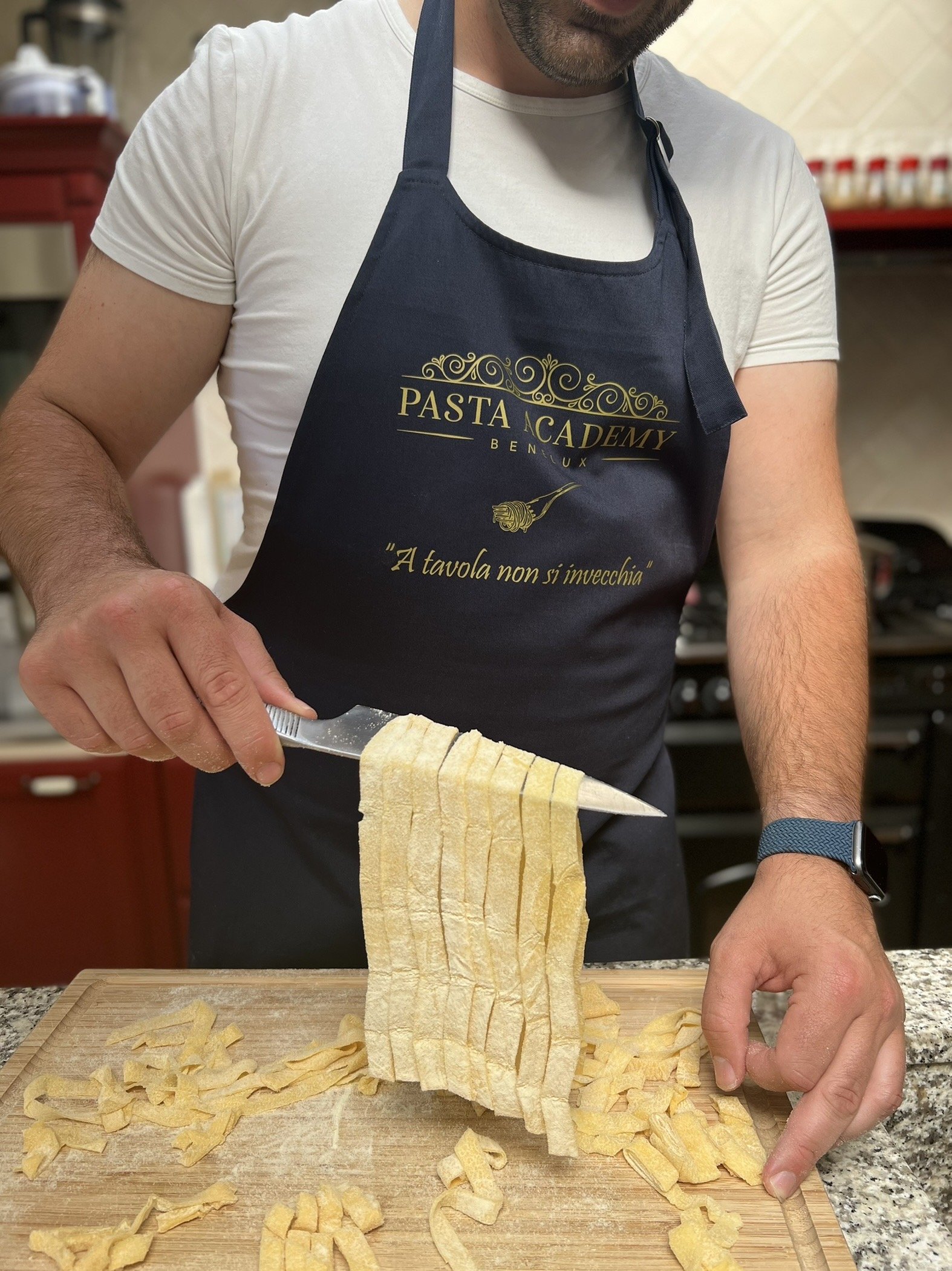 Man met keukenschort aan die pasta maakt